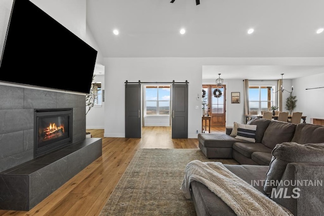 5251 Hidden Hollow Ln, Emmett, ID 83617 - living room featuring a barn door, plenty of natural light, light wood finished floors, a tile fireplace, and vaulted ceiling