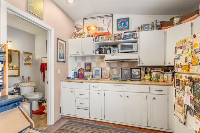 kitchen with lofted ceiling, stainless steel gas stovetop, white cabinets, light tile patterned flooring, and white fridge