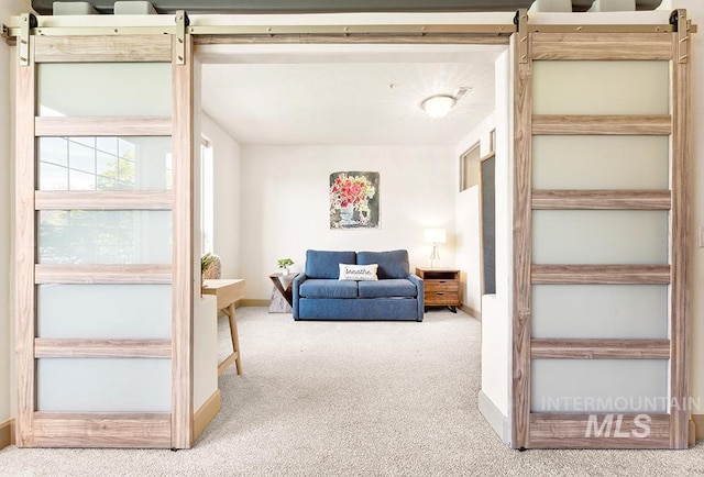 living area featuring a barn door, baseboards, and carpet floors
