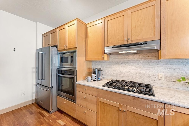 kitchen featuring light wood-type flooring, light brown cabinets, backsplash, under cabinet range hood, and stainless steel appliances