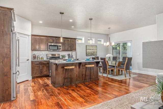 kitchen featuring a textured ceiling, dark wood-type flooring, an inviting chandelier, stainless steel appliances, and a center island with sink