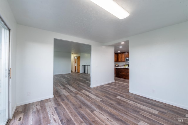 unfurnished living room with dark wood-type flooring, baseboards, and recessed lighting