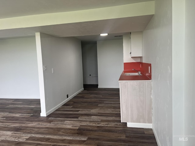 interior space featuring indoor wet bar, baseboards, a sink, and dark wood finished floors