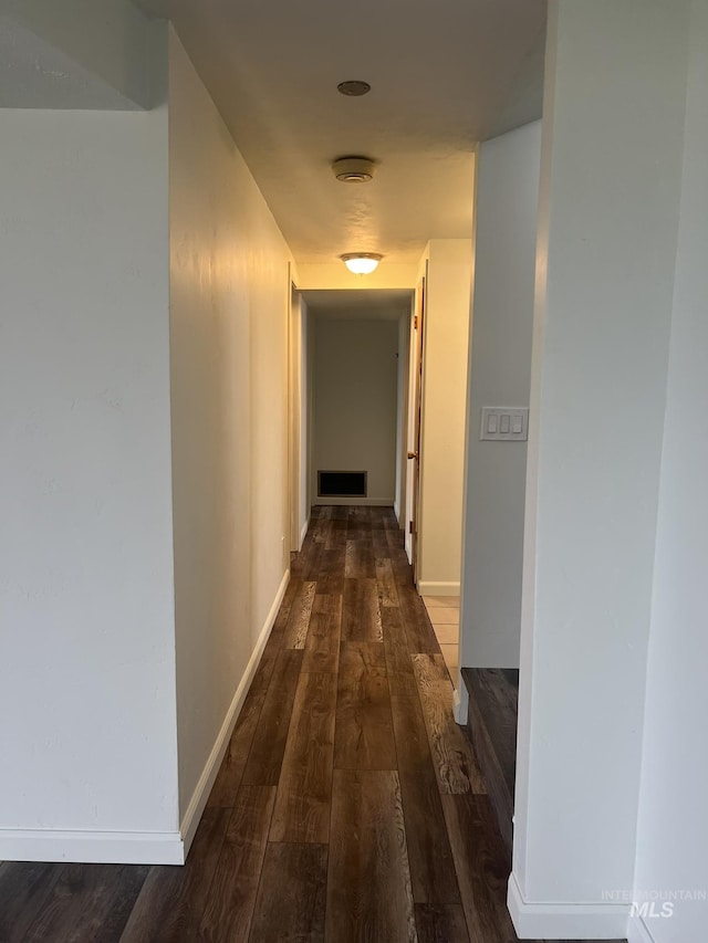 hall with dark wood-type flooring, visible vents, and baseboards