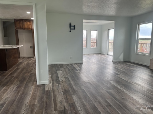 unfurnished living room with a textured ceiling, baseboards, dark wood-style floors, and a wealth of natural light