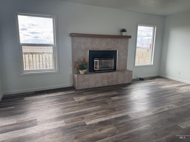 unfurnished living room with dark wood-style flooring, visible vents, baseboards, and a tile fireplace