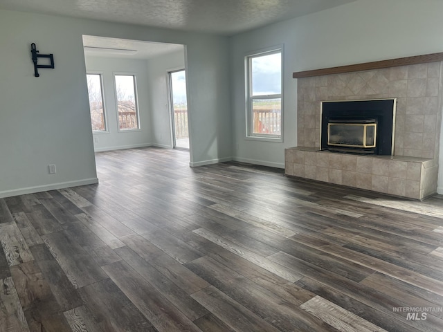 unfurnished living room featuring a tiled fireplace, baseboards, dark wood finished floors, and a textured ceiling