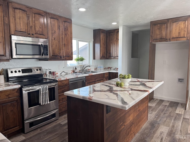 kitchen with a center island, baseboards, a sink, dark wood-style floors, and stainless steel appliances