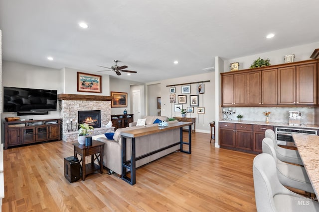 living area featuring a ceiling fan, recessed lighting, a stone fireplace, light wood finished floors, and baseboards