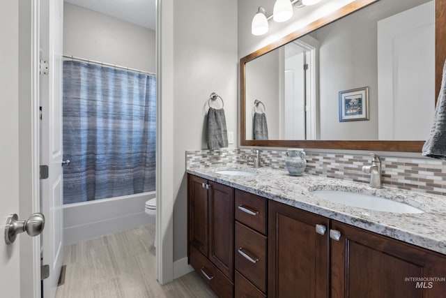 bathroom featuring a sink, backsplash, double vanity, and toilet