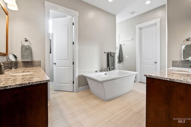 bathroom with a freestanding bath, two vanities, visible vents, and a sink