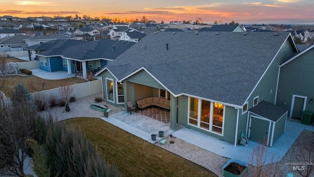 rear view of house featuring a fenced backyard, a yard, a residential view, a shingled roof, and a patio area