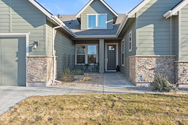 doorway to property with stone siding, an attached garage, and a shingled roof