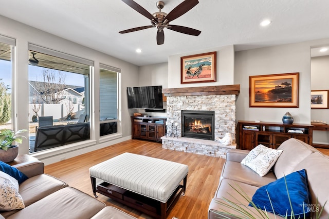 living room featuring wood finished floors, baseboards, recessed lighting, ceiling fan, and a stone fireplace