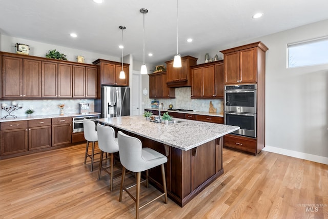 kitchen with light wood finished floors, backsplash, a breakfast bar area, an island with sink, and stainless steel appliances