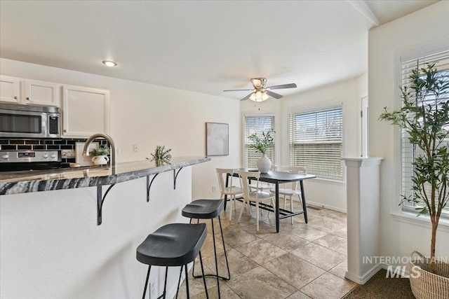 kitchen with a breakfast bar area, baseboards, ceiling fan, stainless steel appliances, and backsplash