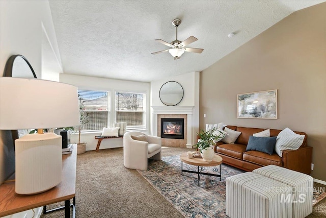 living room with a ceiling fan, carpet floors, vaulted ceiling, a textured ceiling, and a tiled fireplace