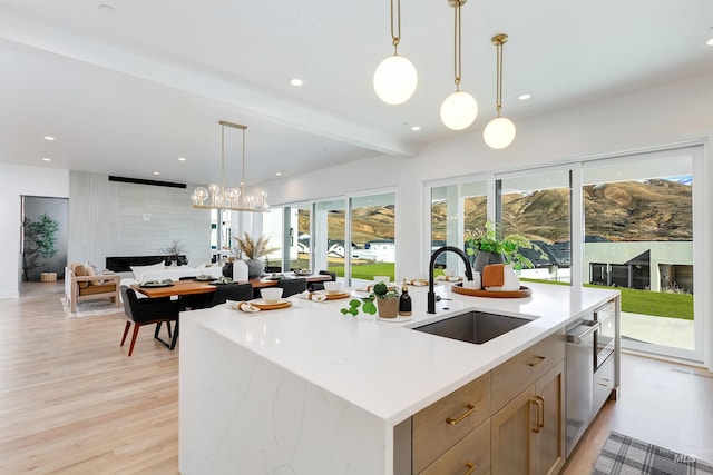 kitchen featuring an island with sink, open floor plan, light wood-type flooring, a sink, and recessed lighting