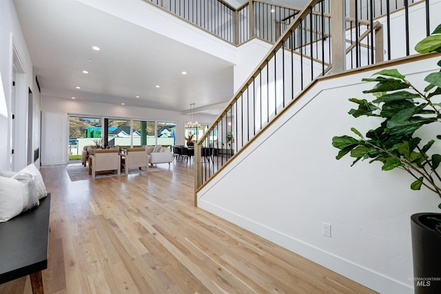 living room featuring a notable chandelier, a high ceiling, wood finished floors, baseboards, and stairs