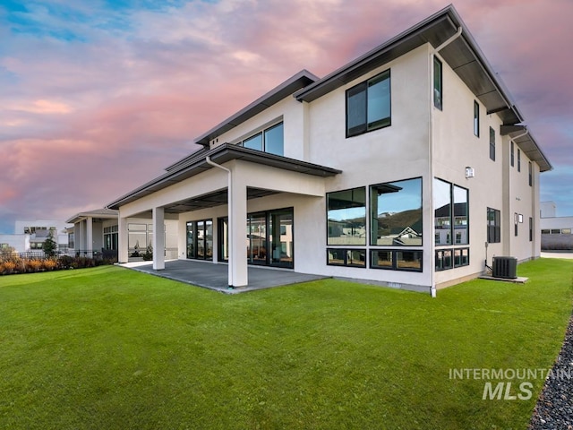 back of property at dusk with a patio, a lawn, cooling unit, and stucco siding