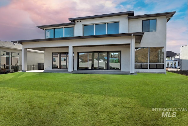 back of property at dusk with a lawn and stucco siding