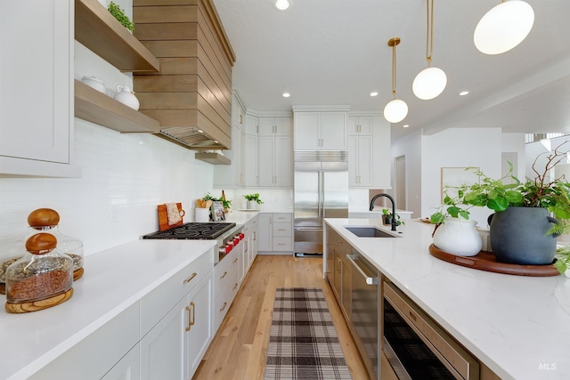 kitchen with stainless steel appliances, decorative backsplash, white cabinetry, a sink, and light wood-type flooring