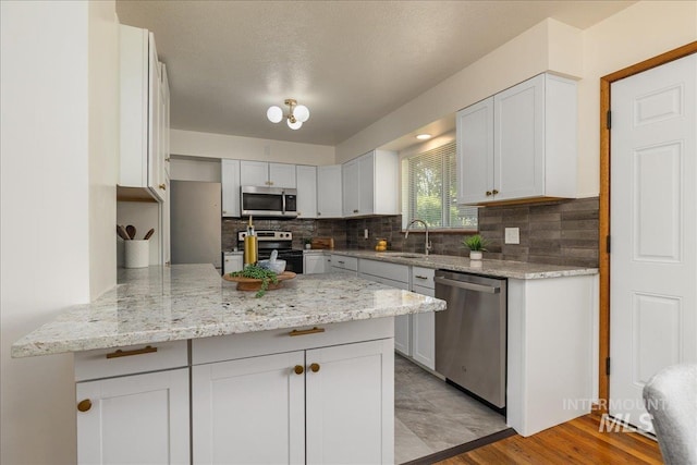 kitchen with sink, stainless steel appliances, light stone counters, white cabinets, and kitchen peninsula