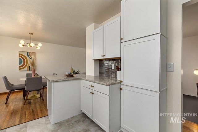 kitchen with white cabinetry, hanging light fixtures, light stone countertops, decorative backsplash, and kitchen peninsula