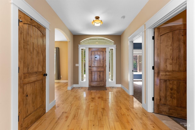 entryway featuring light wood-style floors, arched walkways, and baseboards