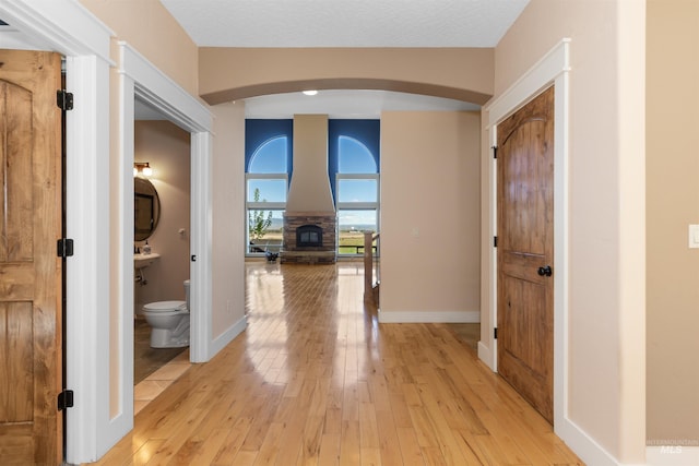 corridor with arched walkways, baseboards, and light wood-style floors