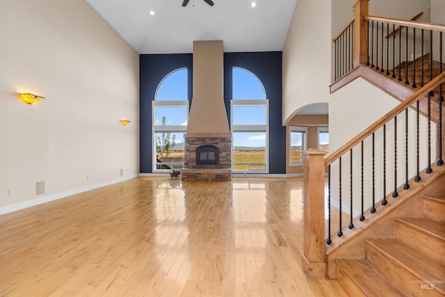 unfurnished living room featuring plenty of natural light, a high ceiling, a ceiling fan, and wood finished floors