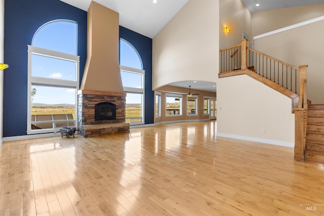 unfurnished living room with high vaulted ceiling, a stone fireplace, baseboards, wood finished floors, and stairway