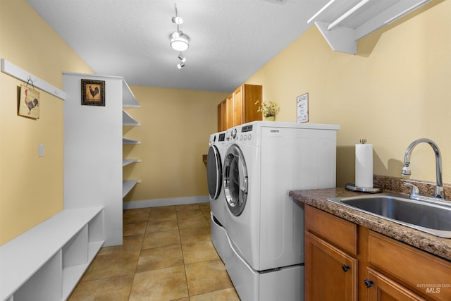 clothes washing area with a textured ceiling, washing machine and clothes dryer, a sink, cabinet space, and light tile patterned floors