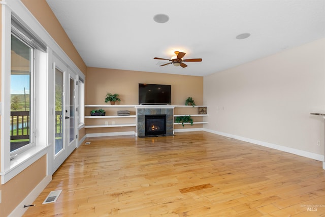 unfurnished living room featuring ceiling fan, light wood finished floors, a tiled fireplace, baseboards, and visible vents