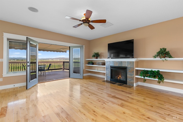 unfurnished living room with a tiled fireplace, baseboards, ceiling fan, and wood finished floors