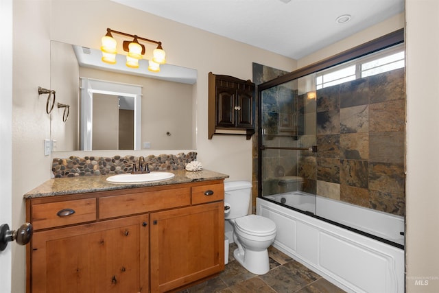 full bath with vanity, combined bath / shower with glass door, toilet, and stone finish flooring