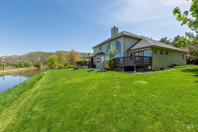 rear view of property with a lawn, a deck with water view, and a chimney