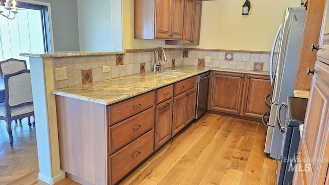 kitchen featuring a sink, stainless steel appliances, brown cabinetry, light stone countertops, and light wood finished floors