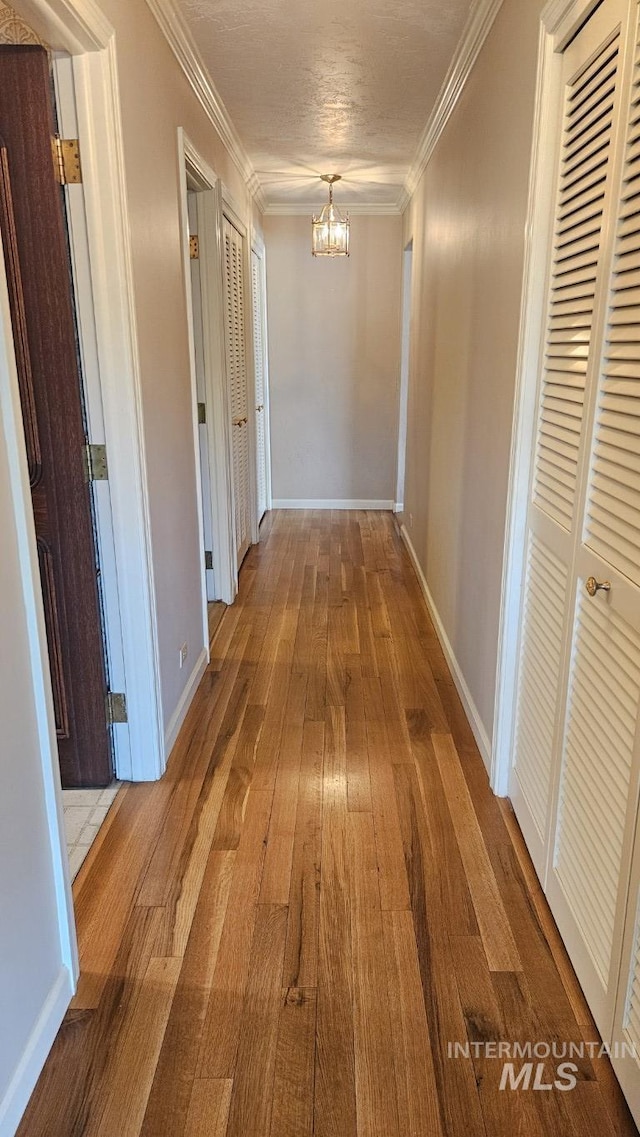 corridor with a chandelier, wood-type flooring, crown molding, and baseboards
