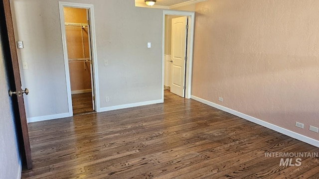 unfurnished bedroom featuring dark wood-style flooring, a walk in closet, a closet, baseboards, and crown molding