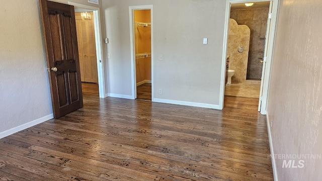 unfurnished bedroom with a spacious closet, wood finished floors, a closet, baseboards, and ensuite bathroom