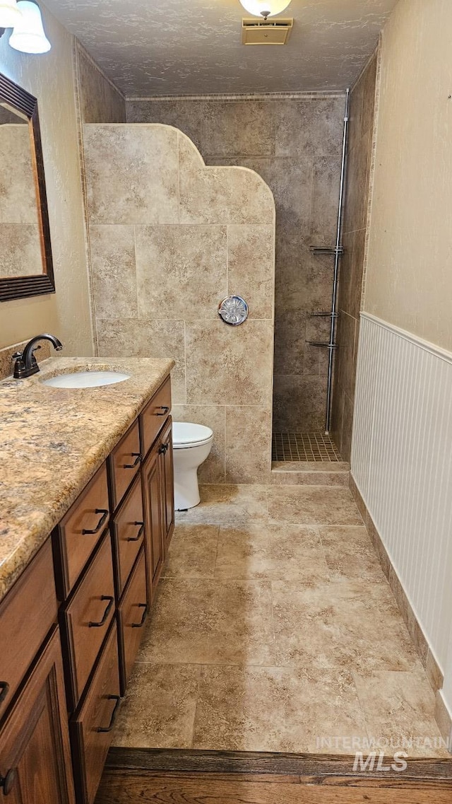 full bathroom with a tile shower, toilet, and vanity