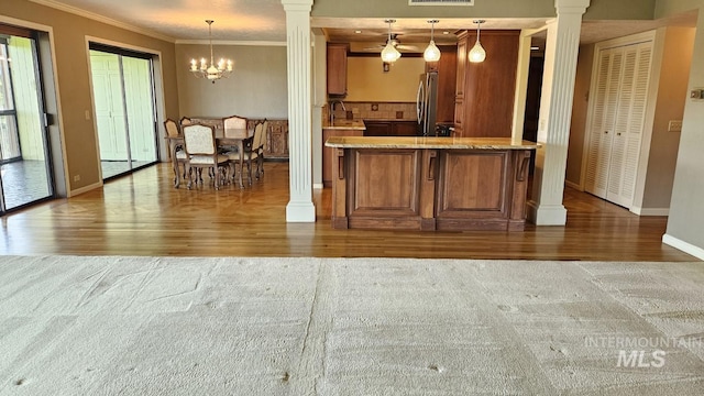 kitchen featuring wood finished floors, brown cabinets, ornate columns, baseboards, and ornamental molding