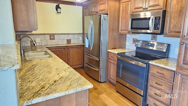 kitchen featuring stainless steel appliances, a sink, backsplash, light stone countertops, and brown cabinets