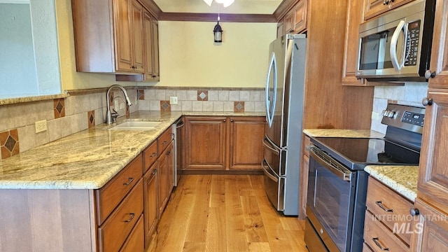 kitchen with stainless steel appliances, a sink, decorative backsplash, brown cabinetry, and crown molding