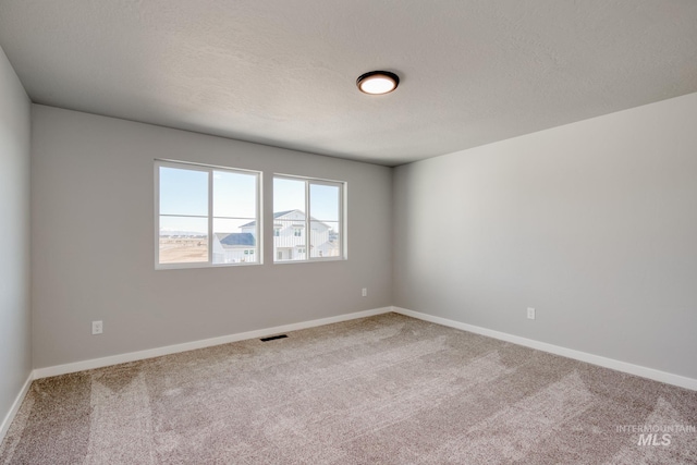 spare room with carpet flooring, visible vents, baseboards, and a textured ceiling