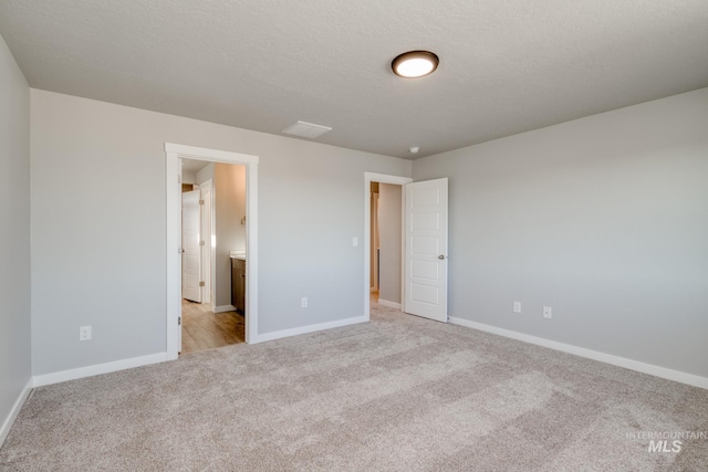 unfurnished bedroom with baseboards, light carpet, a textured ceiling, and connected bathroom