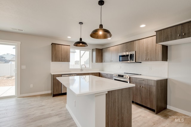 kitchen with light wood finished floors, a sink, appliances with stainless steel finishes, backsplash, and a center island