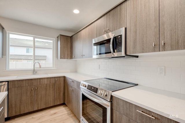 kitchen with backsplash, light countertops, light wood-style floors, stainless steel appliances, and a sink