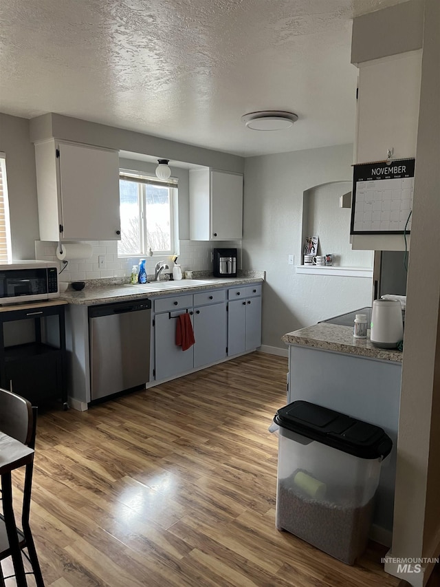 kitchen featuring appliances with stainless steel finishes, a textured ceiling, sink, light hardwood / wood-style floors, and white cabinetry